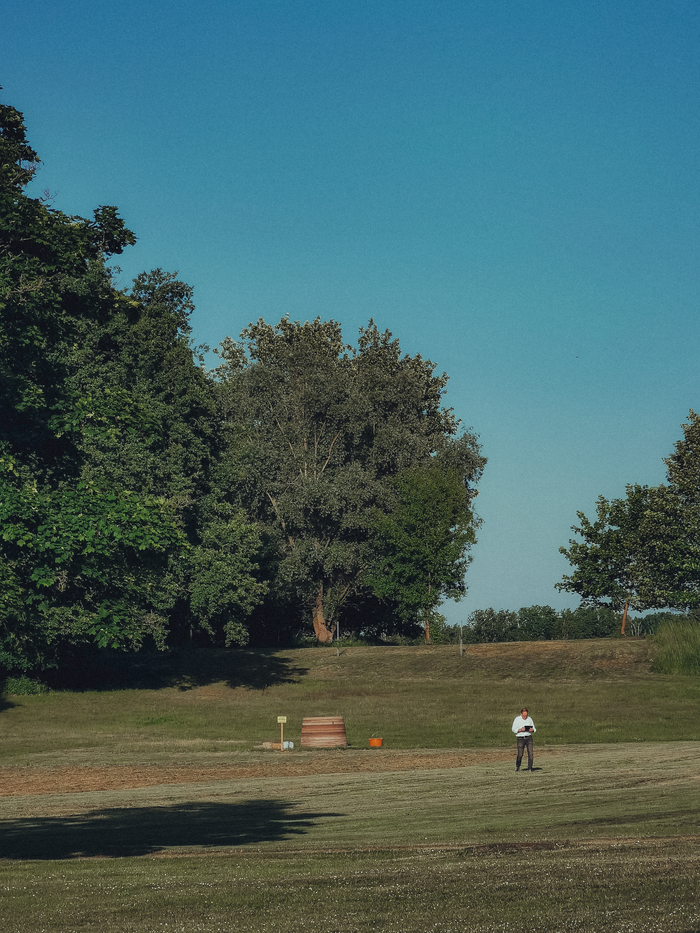 A person walking in a sunny park surrounded by lush greenery and clear blue sky.