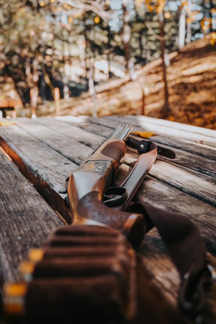 Artistic view of a shotgun resting on a wooden table amidst an outdoor forest setting.