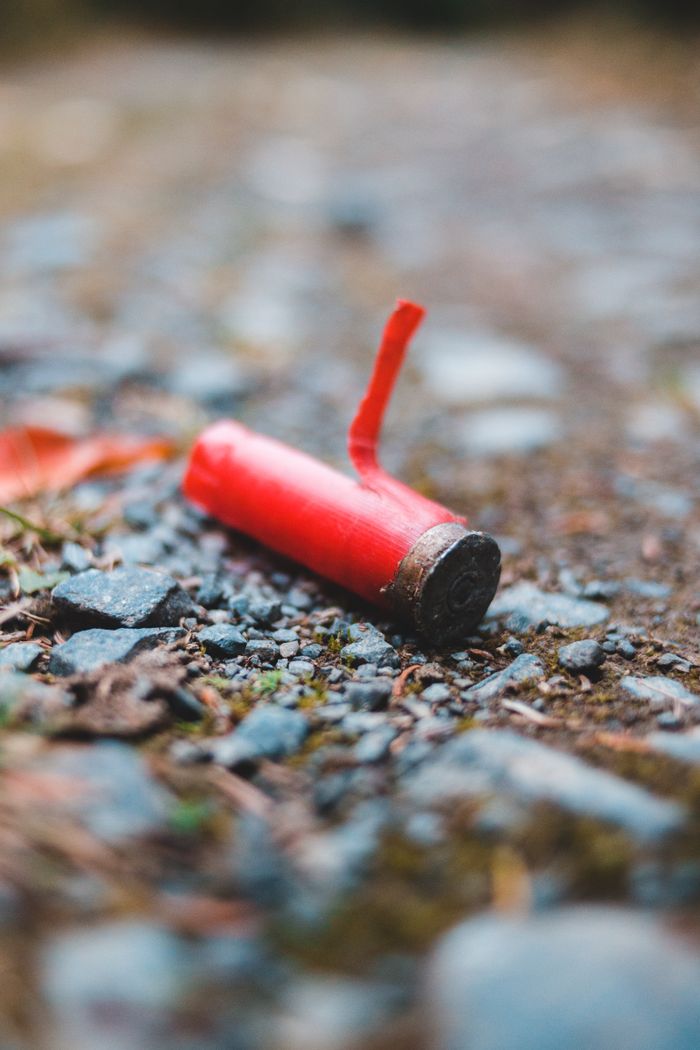 Red used bullet from rifle placed on rough terrain with stones in soft focus