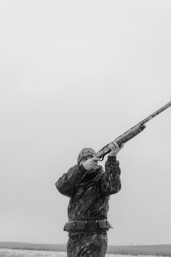 Hunter in camouflage aiming a rifle in the countryside, monochrome shot.