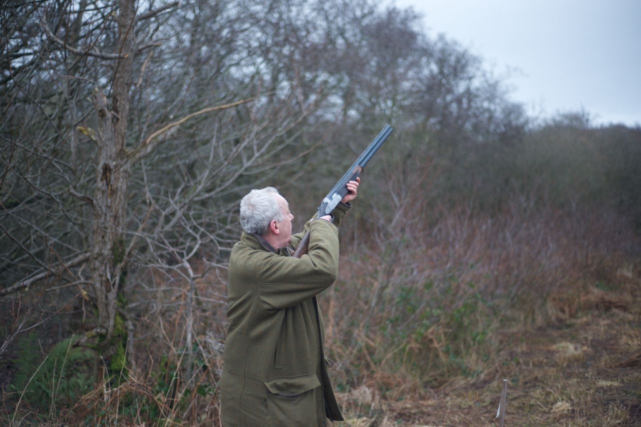 Hunter with shotgun aiming in a wooded area in Lytham St Annes, England.